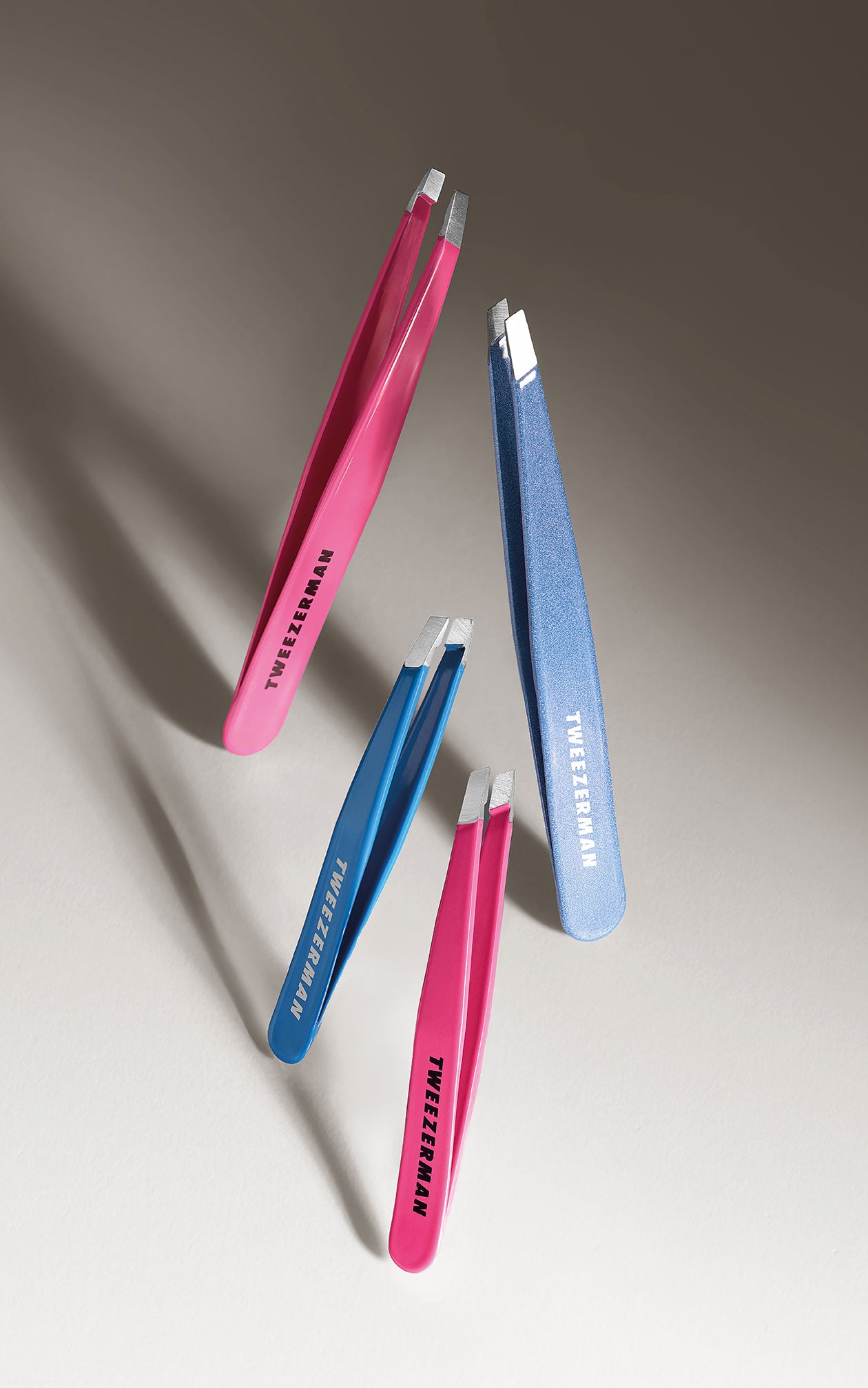 Tweezerman-Pinzetten in Blau und Pink, schwebend vor beige-grauem Hintergrund