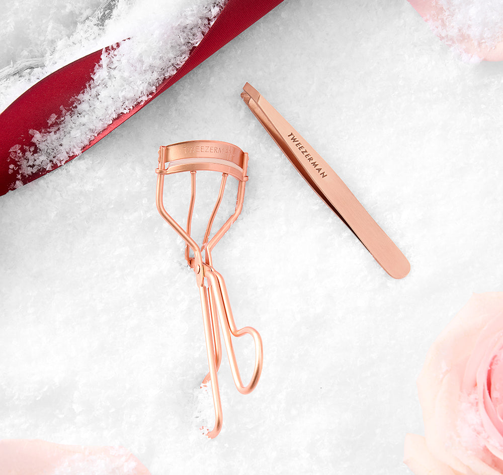 Rose Gold Wimpern Curler und Tweezer vor festlichem Hintergrund – perfekte Beauty Tools für glamouröse Augenblicke in der Holiday Season.