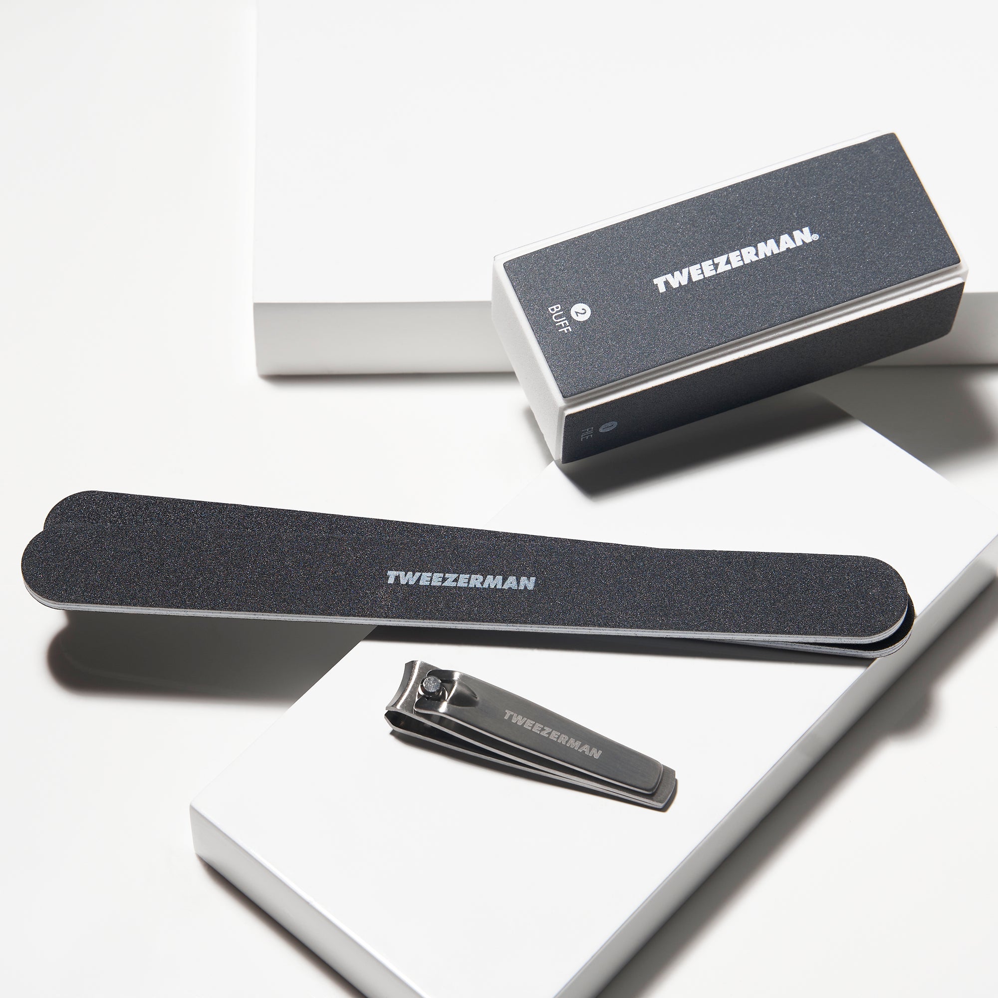 TWEEZERMAN 4teiliges Set, mit essentiellen Produkten auf weißen Podesten.