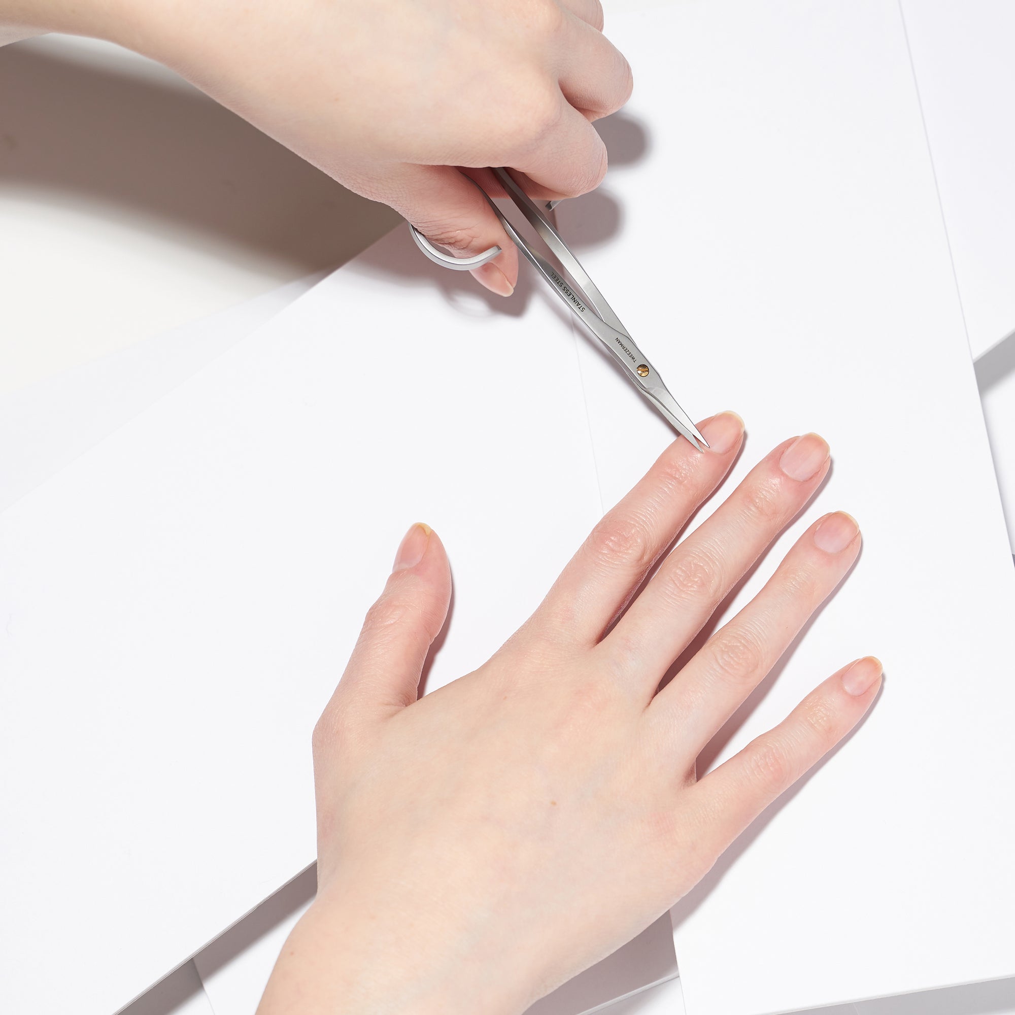 Anwendung einer TWEEZERMAN Nagelhautschere in silber am linken Mittelfinger.