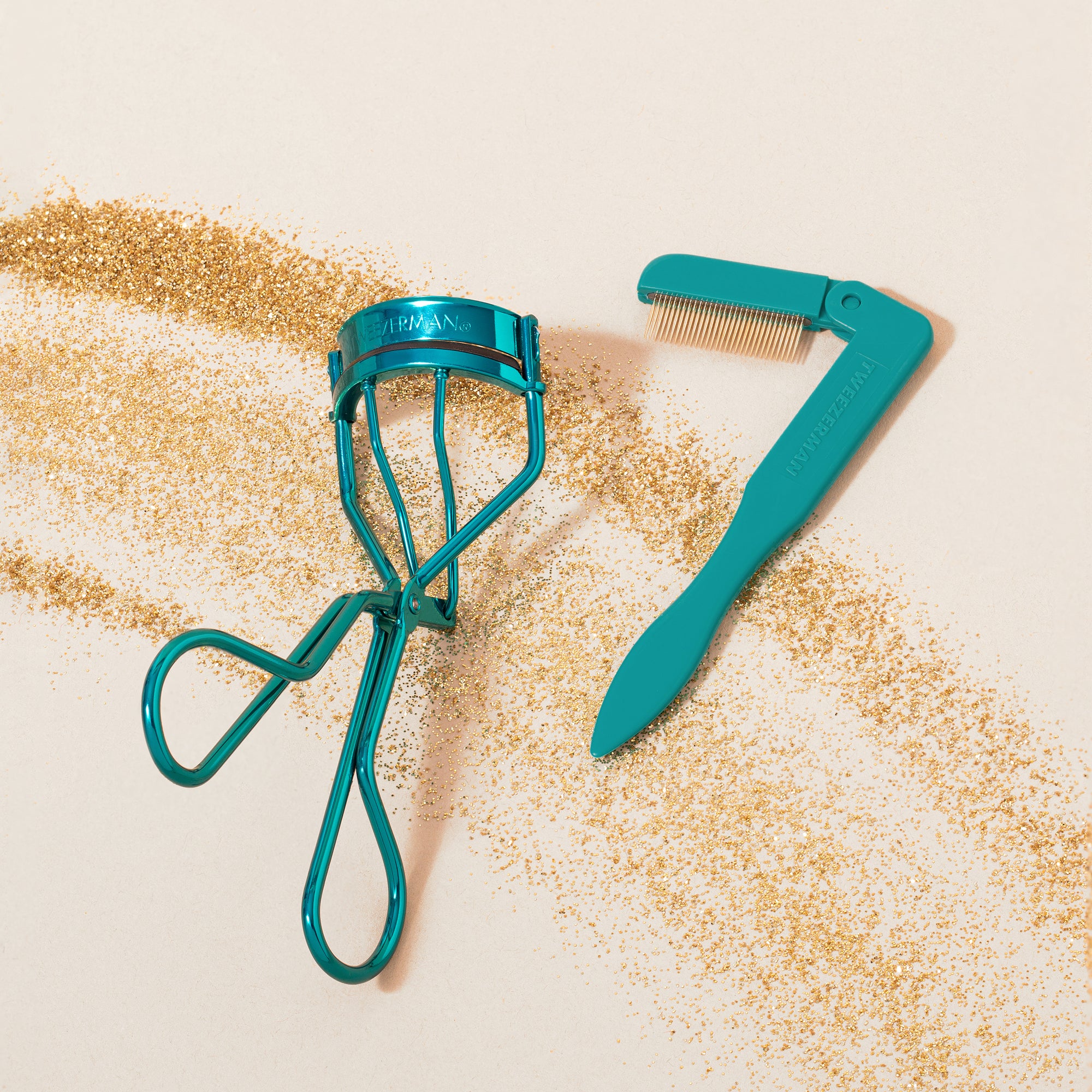 TWEEZERMAN Set mit klassicher Wimpernzange und faltbarem Wimpernkamm in türkis auf weißen Hintergrund mit goldenem Glitzer.
