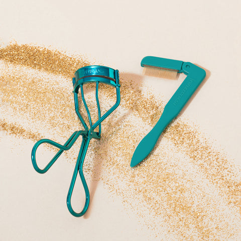 TWEEZERMAN Set mit klassicher Wimpernzange und faltbarem Wimpernkamm in türkis auf weißen Hintergrund mit goldenem Glitzer.