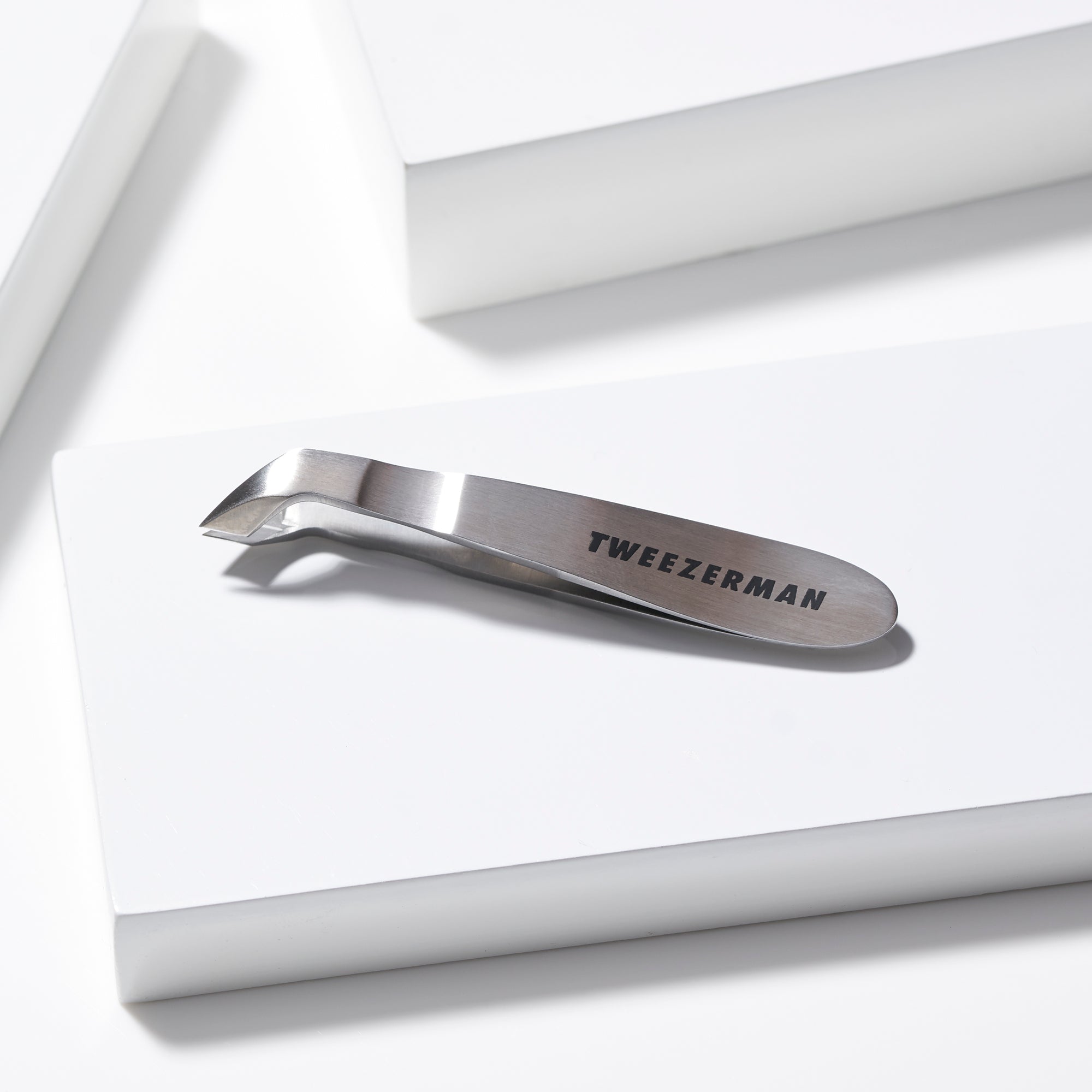 TWEEZERMAN Mini Nagelhautschneider in silber aus rostfreiem Edelstahl mit scharfen und robusten Schneiden auf weißen Podesten.