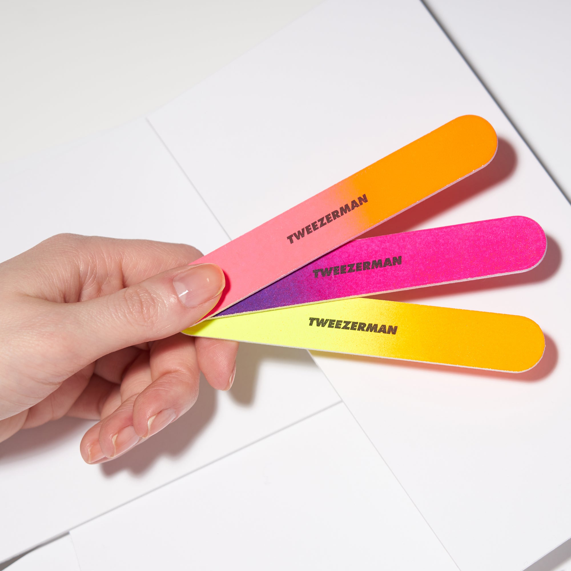 Drei TWEEZERMAN Nagelfeilen in verschiedenen Neonfarben, mit zwei unterschiedlichen Anwendungsflächen in der linken Hand.