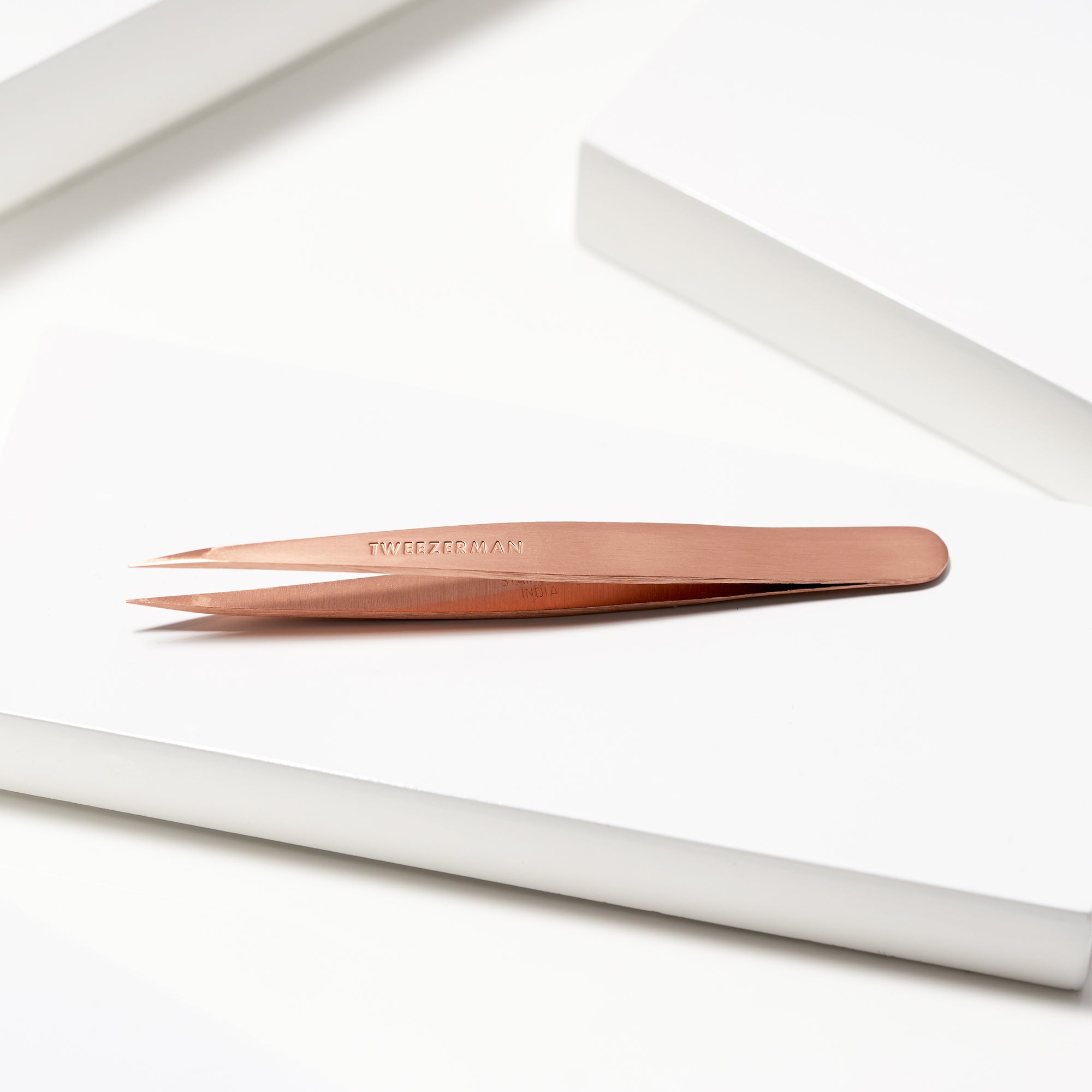 TWEEZERMAN spitze Pinzette in rose gold liegend auf weißen Podesten.