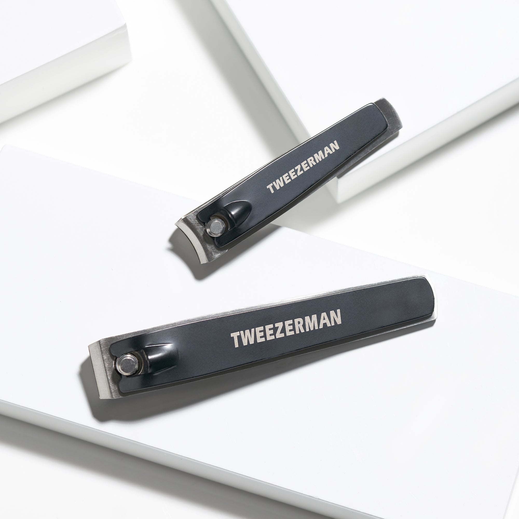 TWEEZERMAN Nagelknipser Set mit zwei Nagelknipsern in silber/schwarz aus rostfreiem Edelstahl, auf weißen Podesten.