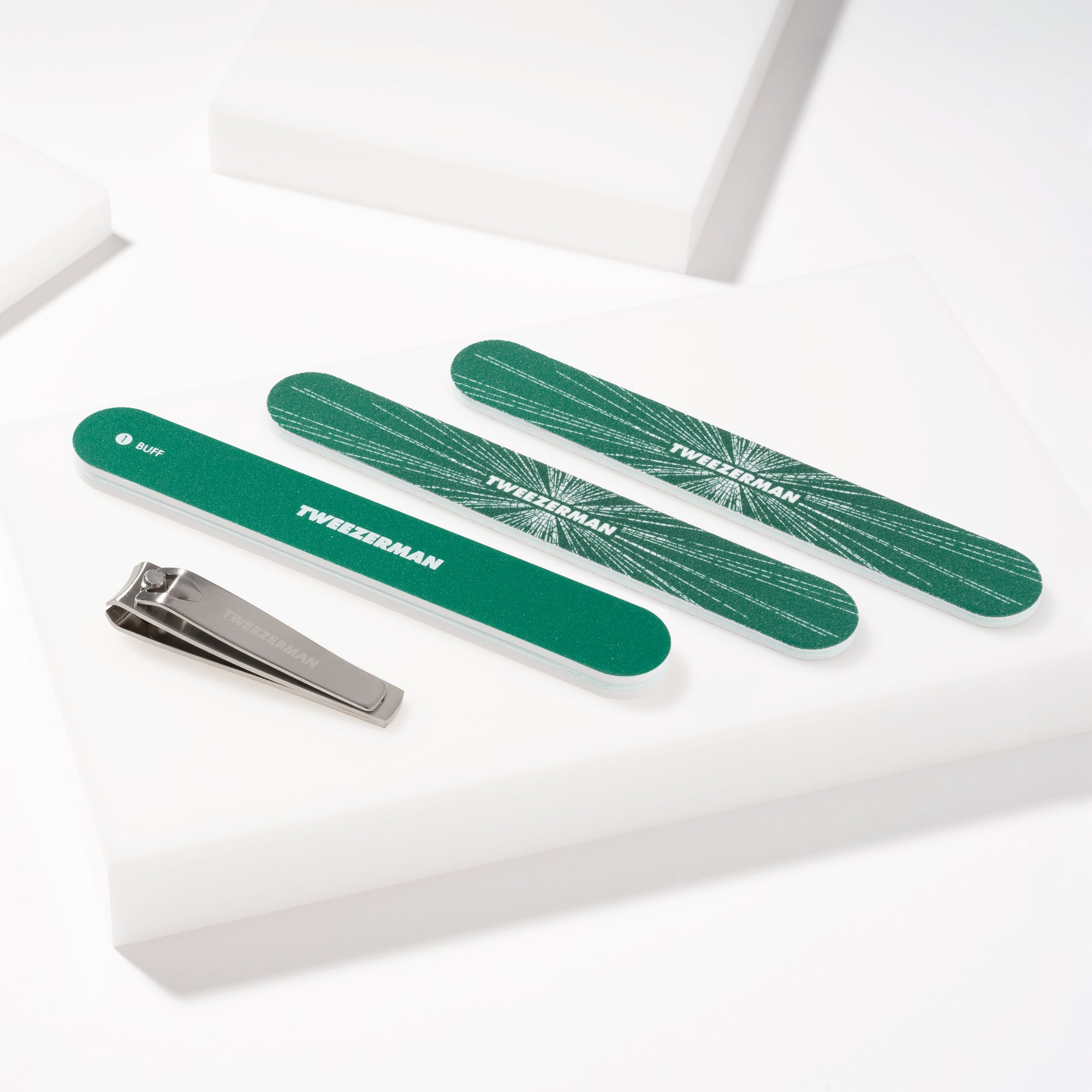 TWEEZERMAN Geschenkset mit verschiedenen Produkten aus rostfreiem Edelstahl speziell für die Nagelpflege auf weißen Podesten.