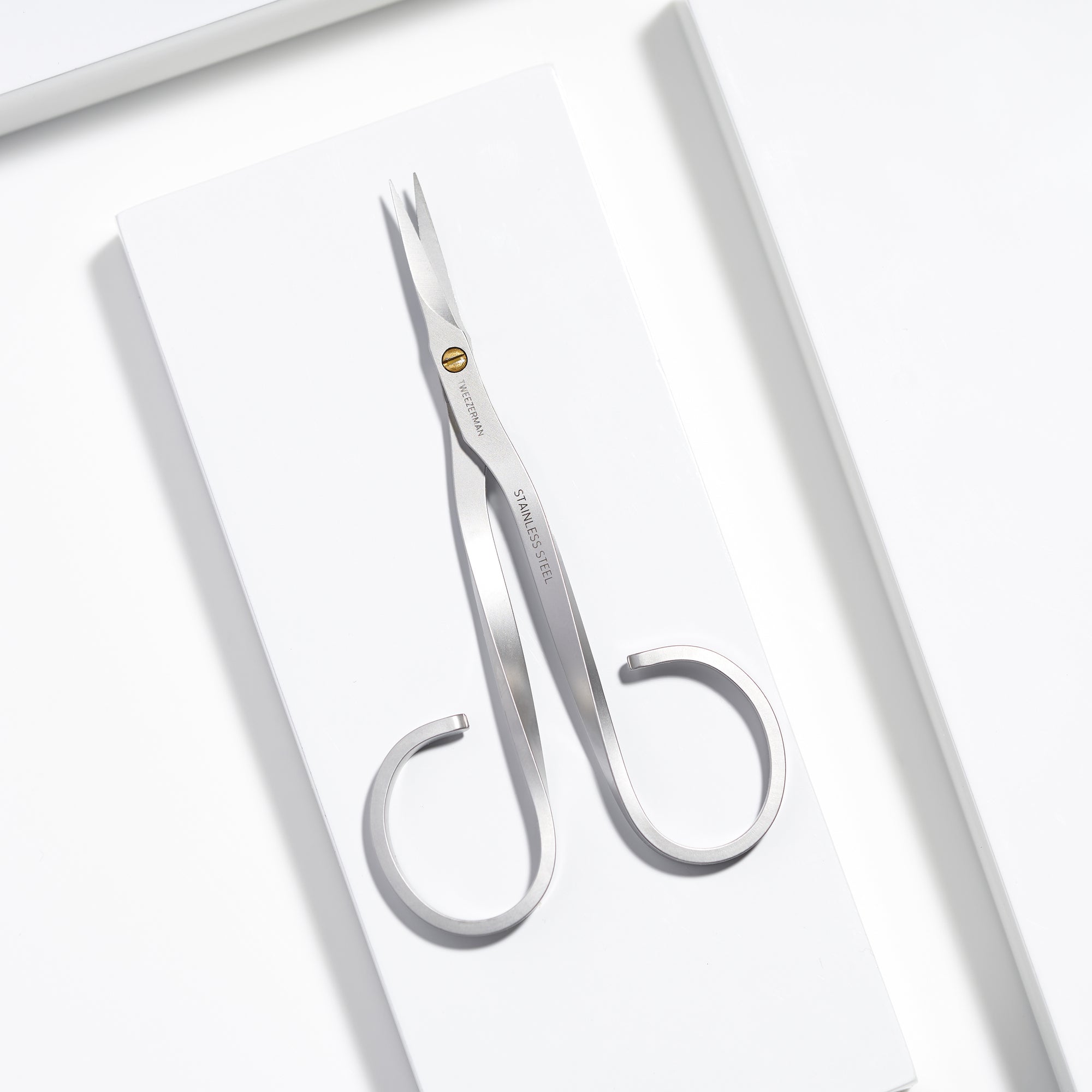 TWEEZERMAN Nagelhautschere in silber aus rostfreiem Edelstahl mit scharfen Präzisionsschneiden auf weißen Podesten.