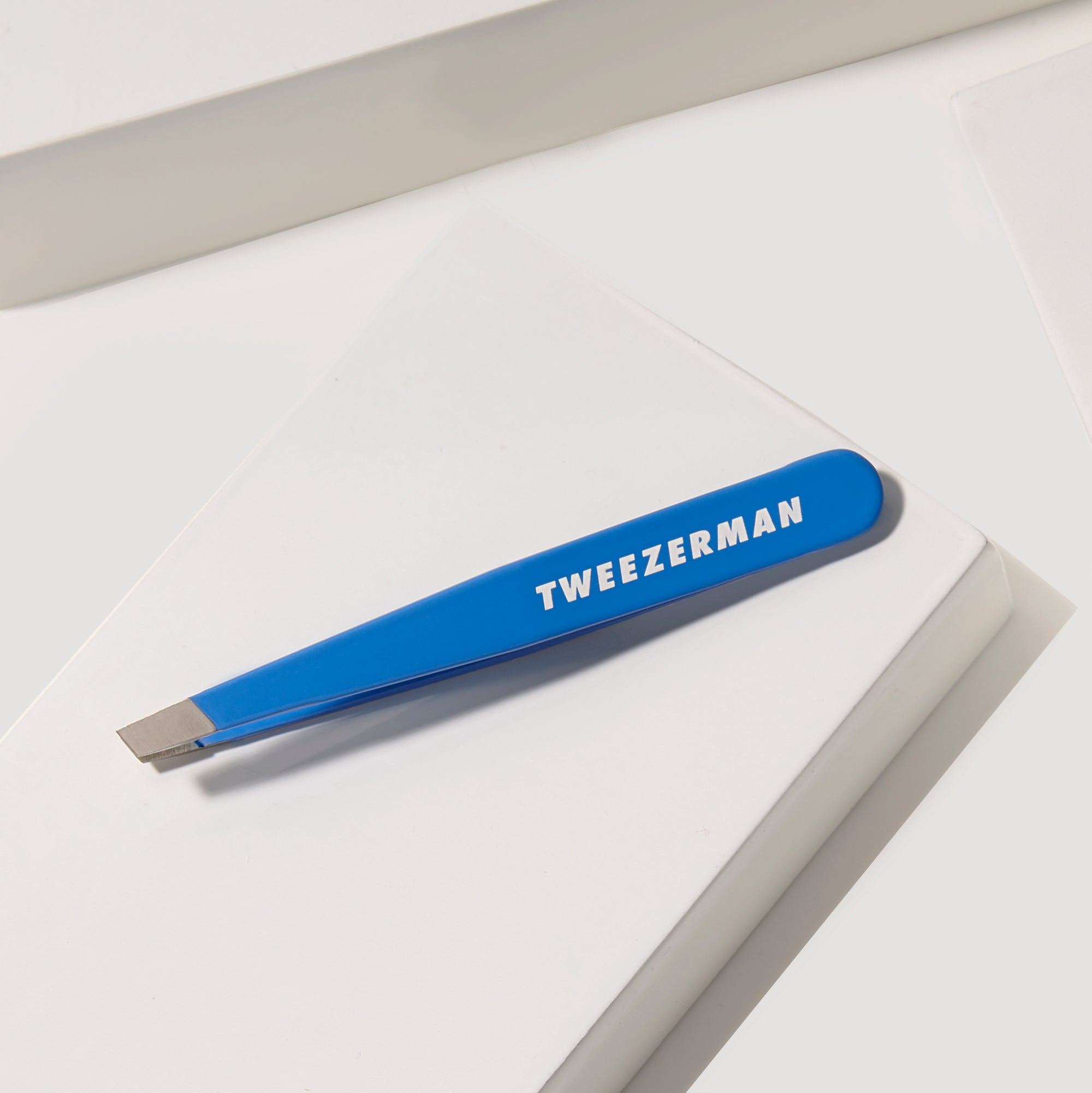 TWEEZERMAN schräge Pinzette in blau liegend auf weißen Podesten.