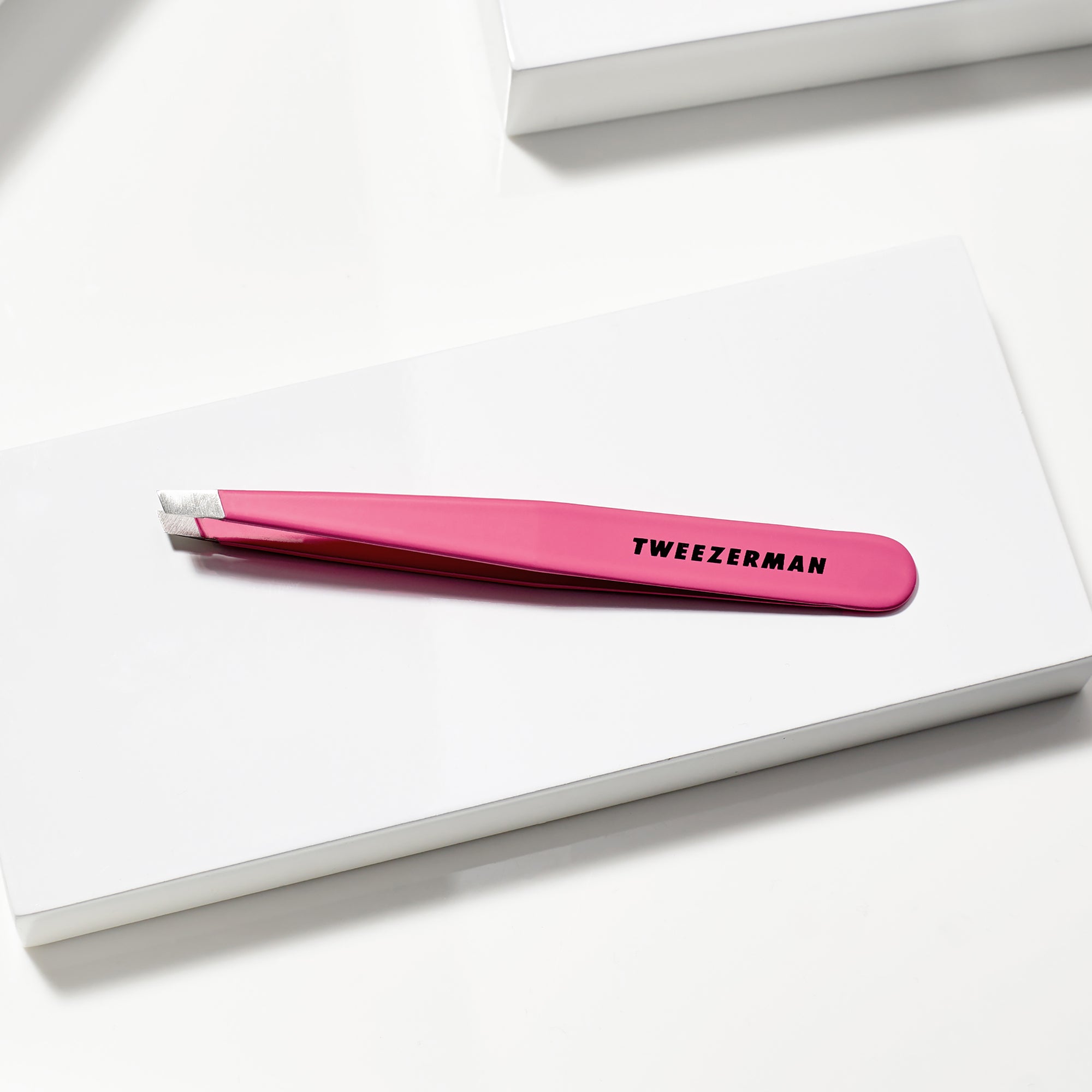 TWEEZERMAN schräge Pinzette in pink liegend auf weißen Podesten.