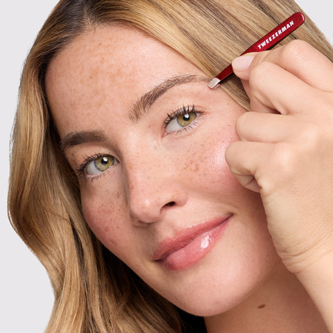 Anwendung einer TWEEZERMAN Schrägen Mini Pinzette in Dunkelrot am linken Auge mit der linken Hand.