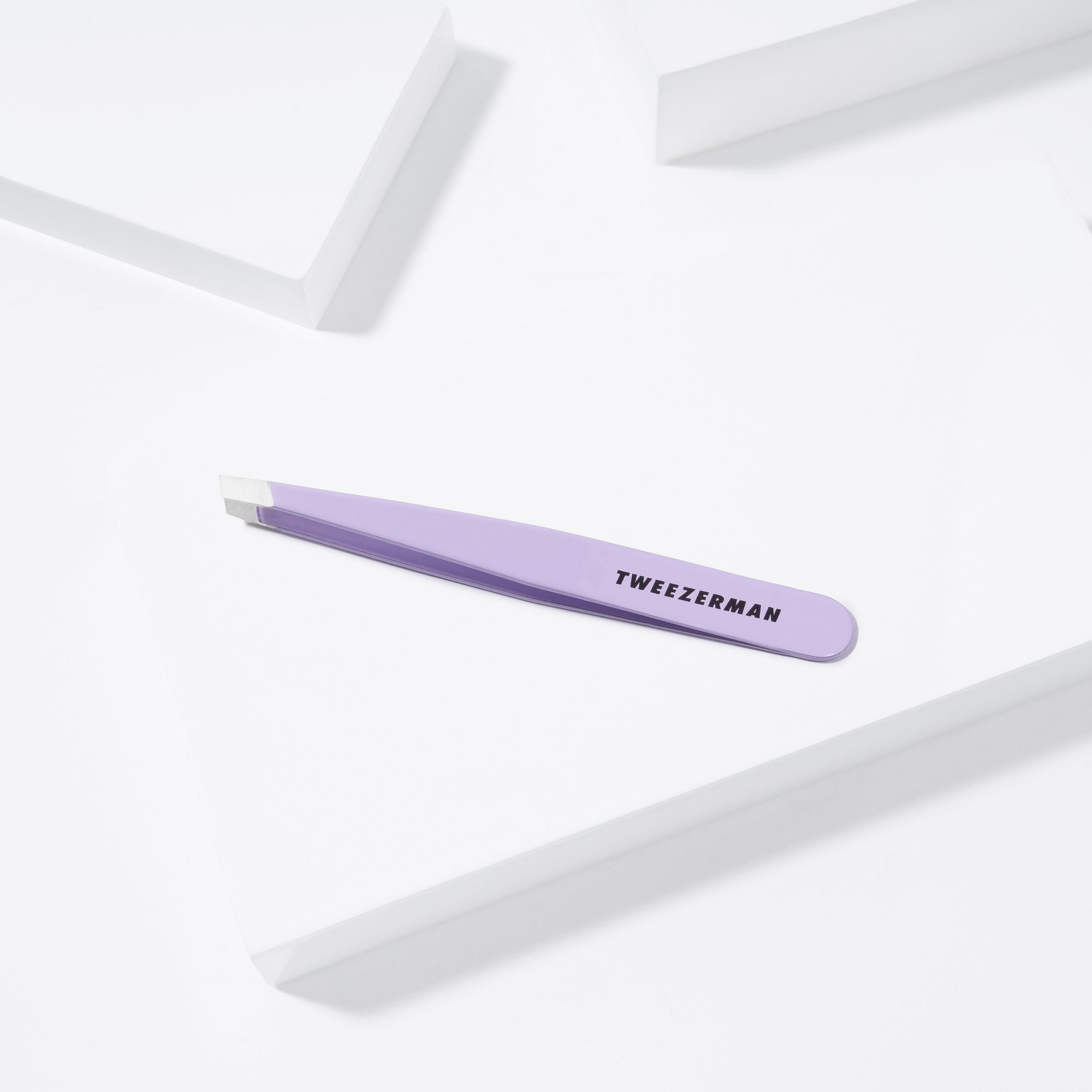 TWEEZERMAN schräge Pinzette in lavender liegend auf weißen Podesten.
