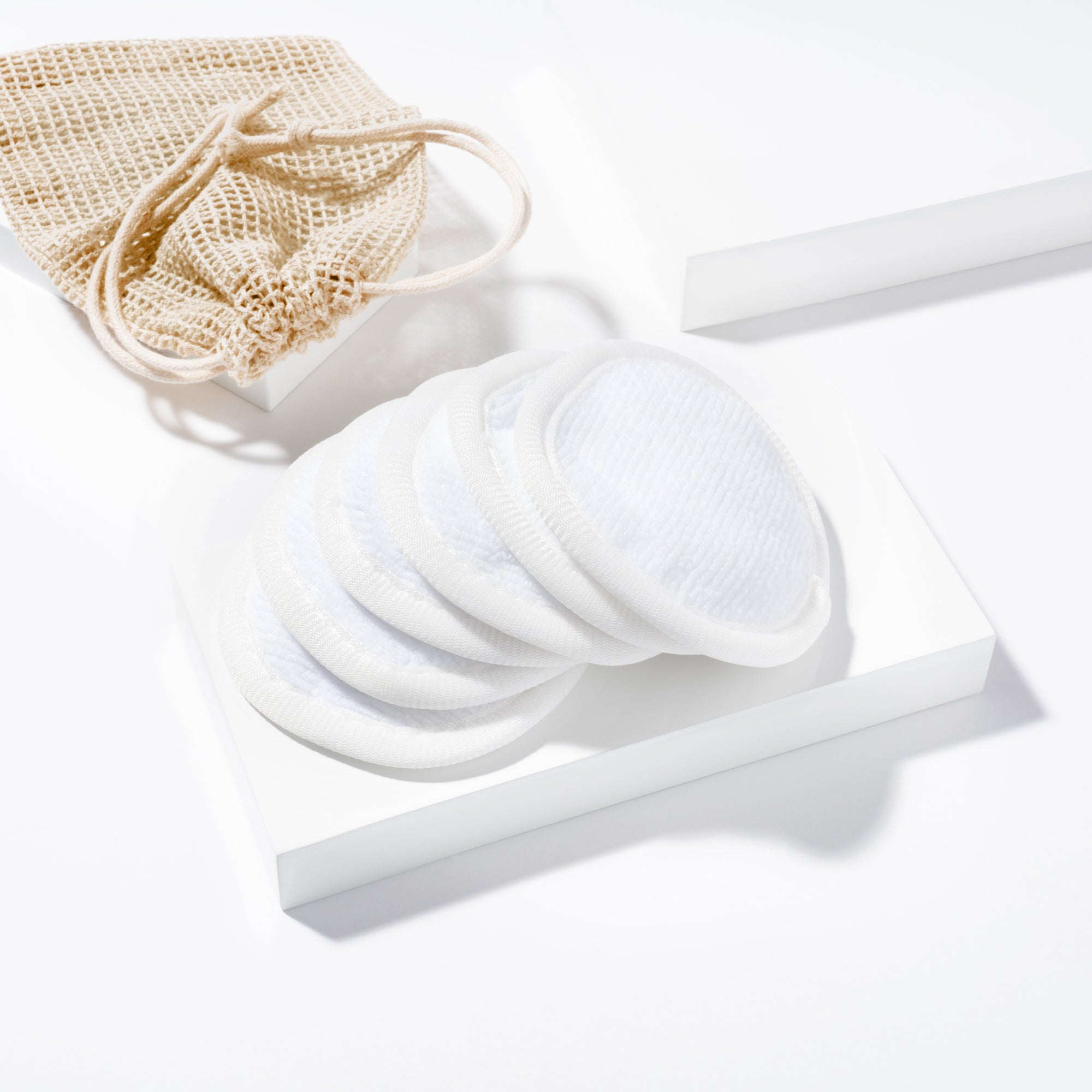 TWEEZERMAN wiederverwendbare MakeUp Entferner Pads inklusive Beutel für die Aufbewahrung auf weißen Podesten.