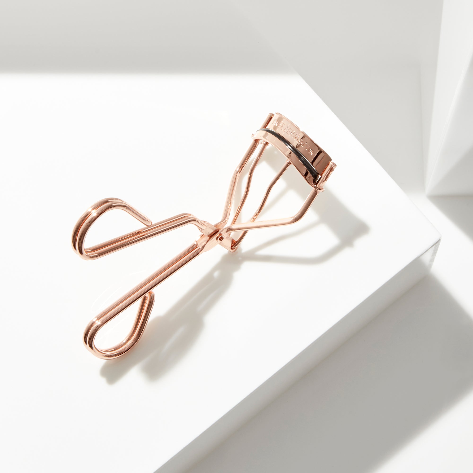 TWEEZERMAN ProCurl Wimpernzange in der Farbe rose gold auf weißen Podesten.
