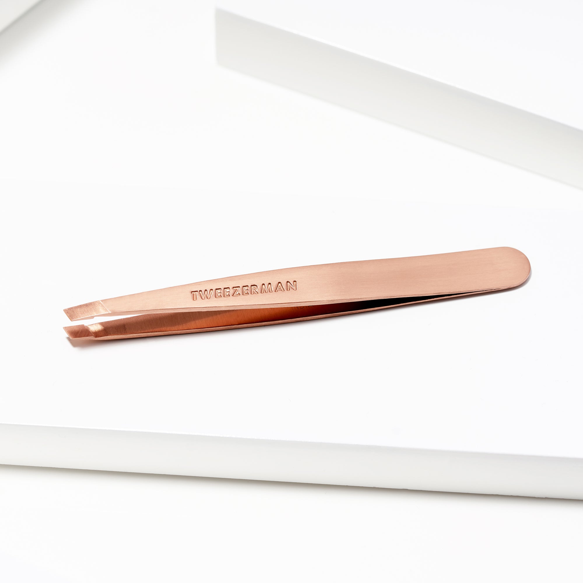 TWEEZERMAN schräge Pinzette in rose gold liegend auf weißen Podesten.