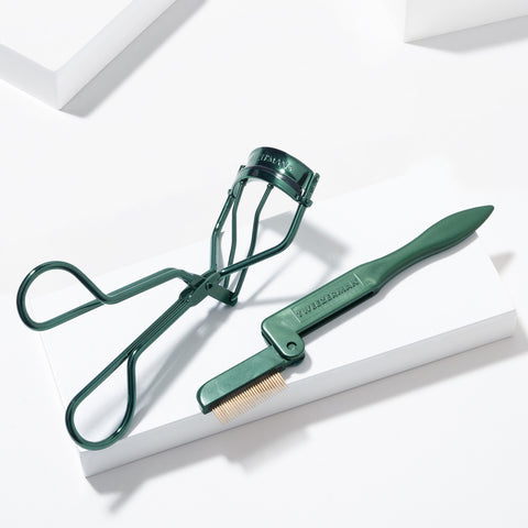 TWEEZERMAN Geschenkset mit klassischer Wimpernzange und Wimpernkamm in grün auf weißen Podesten.